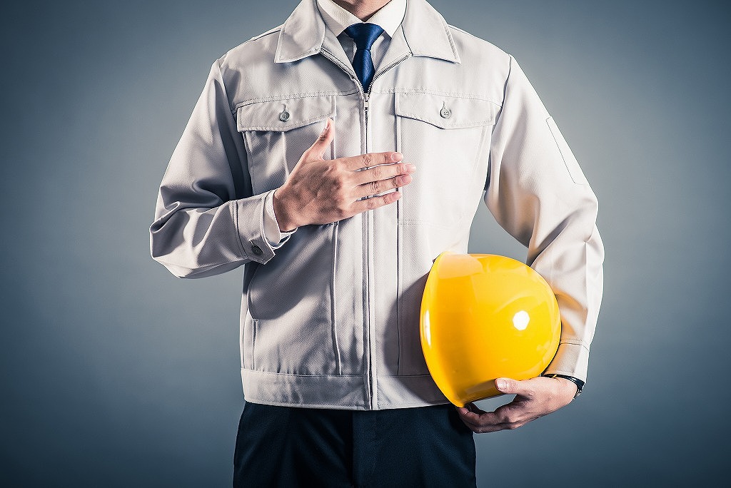 手を胸に当てている作業服の男性